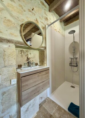 A bathroom with a stone wall, wooden vanity, a round mirror, and a shower. - Clos de La Brelaisiere (CHAUVIGNY)