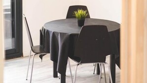Ein Zimmer mit einem runden Tisch, schwarzen Stühlen, einer Topfpflanze, einem flachbildfernseher an der Wand und einer Holzbalkendecke.