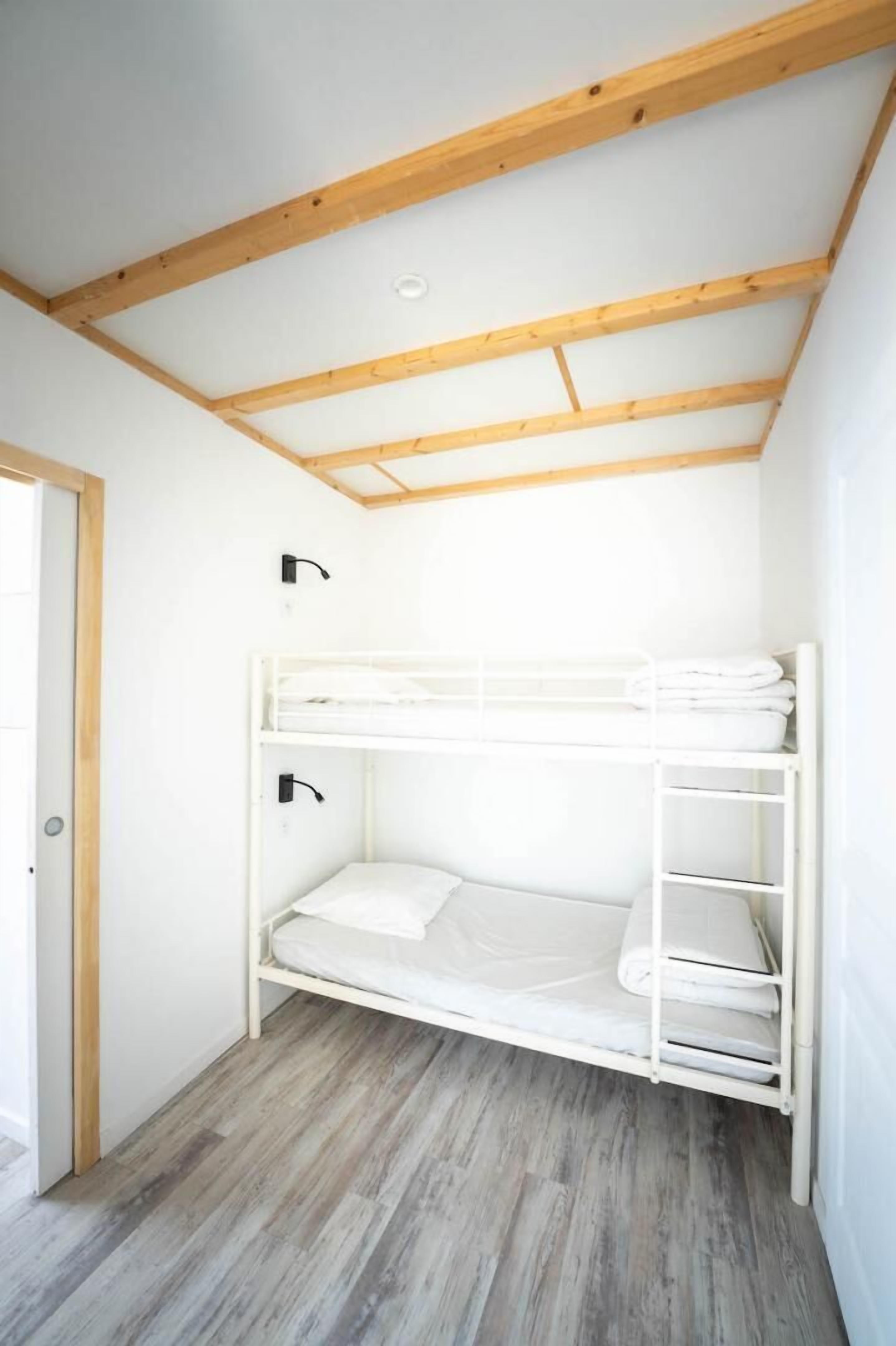 A bunk bed with a wooden ceiling and a door on the left.