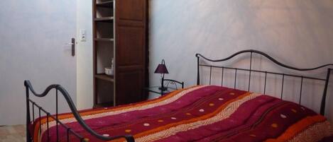 Een slaapkamer met een metalen bed, een houten garderobe en een klein nachtkastje met een lamp.