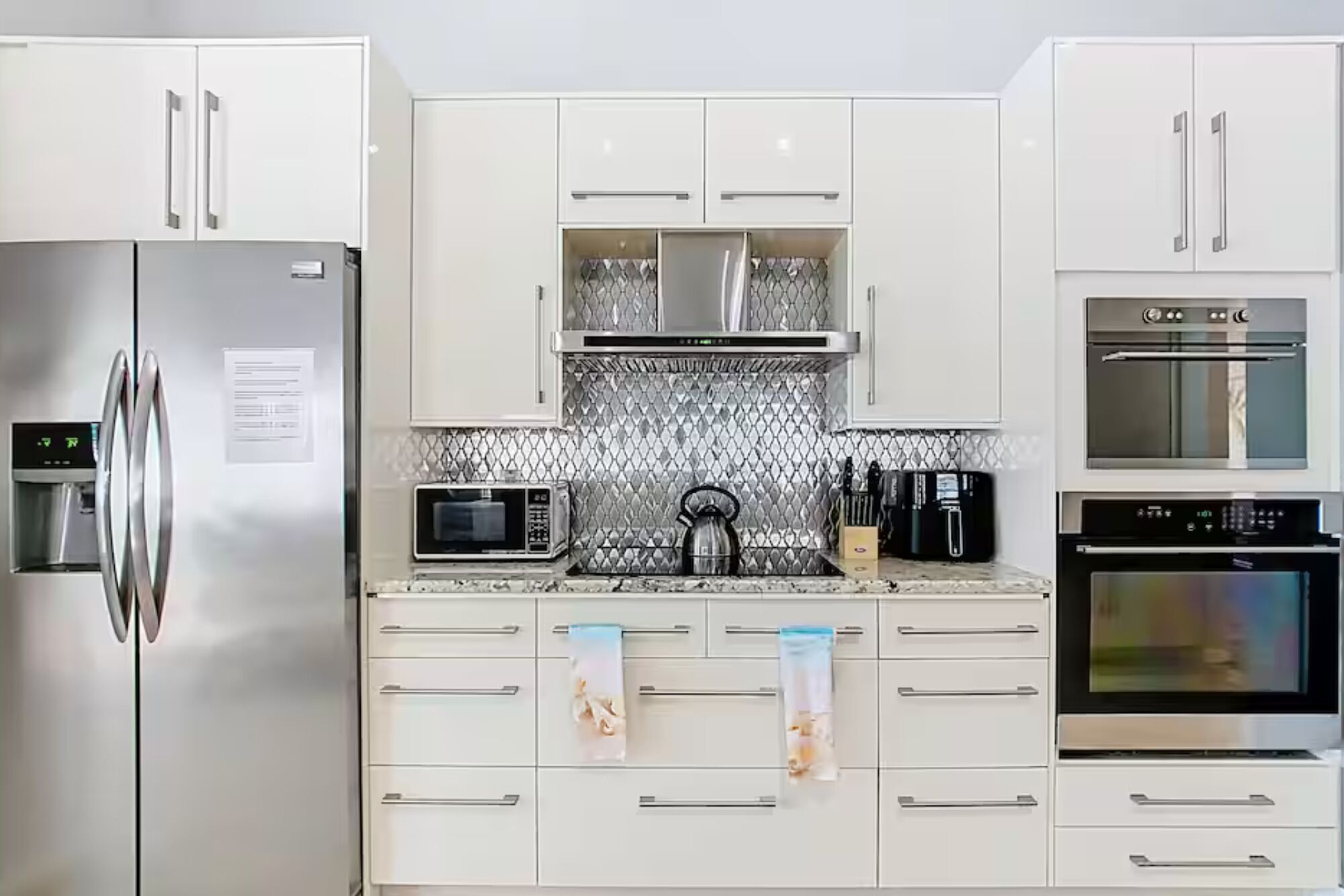 Een keuken met roestvrijstalen apparatuur, witte kasten, een magnetron, waterkoker en koffiezetapparaat.