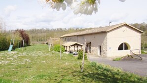 A rustic stone building with a covered outdoor seating area, a swing set, and a paved driveway. - Le Moulin de Chaume - CHAMPAGNE-SAINT-HILAIRE (CHAMPAGNE-SAINT-HILAIRE)