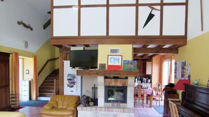 A living room with a fireplace, a television, a piano, and a staircase. - Le Moulin de Chaume - CHAMPAGNE-SAINT-HILAIRE (CHAMPAGNE-SAINT-HILAIRE)