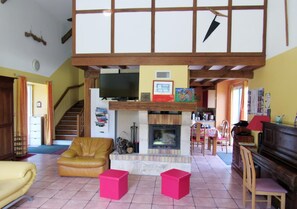 Een woonkamer met een open haard, een televisie, een piano en een trap.