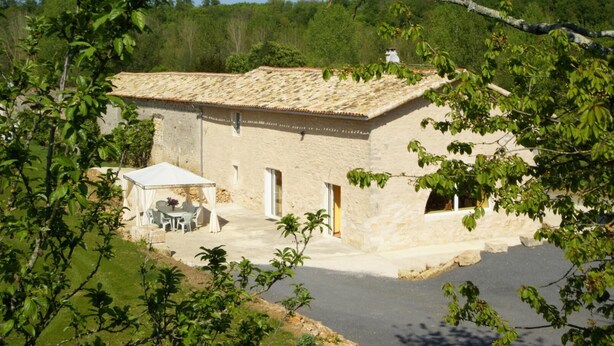 A stone building with a tiled roof, a covered outdoor seating area, and a paved driveway. - Le Moulin de Chaume - CHAMPAGNE-SAINT-HILAIRE (CHAMPAGNE-SAINT-HILAIRE)