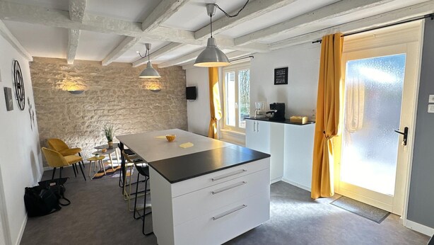 Een compacte keuken met een centraal eiland, een eethoek met gele stoelen, een stenen muur en een deur voorzien van gordijnen.