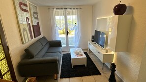 Ein Wohnzimmer mit einer Couch, einem Couchtisch, einem Fernseher und einer Tür mit Vorhängen.