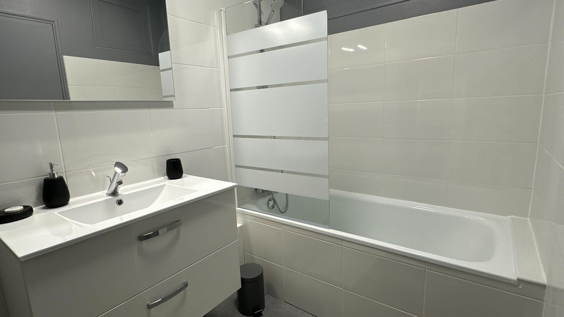 Un baño moderno con lavamanos, espejo y bañera blancos.