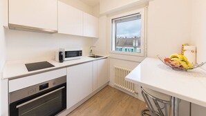 Cocina compacta con armarios blancos, microondas, horno, lavamanos y ventana con vistas.