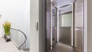 Un ascensor moderno con detalles metálicos, puerta de cristal y barandilla.