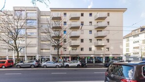 Un edificio de varios pisos con balcones, coches aparcados y cielo despejado.