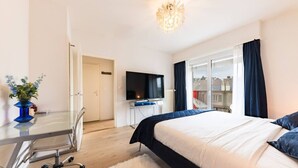 Habitación de hotel con cama, escritorio, silla, televisor y vista al exterior.