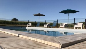 Una piscina con cubierta de madera, dos sombrillas y sillas de descanso.