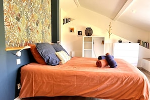 A bedroom with a bed, pillows, a wall art piece, a white dresser, and a shelf with books. - Le Chant du Jau - BEAUMONT SAINT CYR (BEAUMONT SAINT CYR)