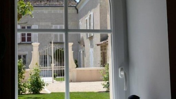 Une fenêtre donnant sur un immeuble et un jardin.