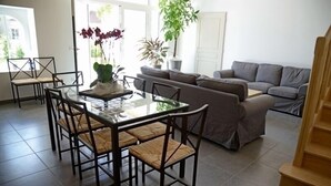 Un coin repas avec une table et des chaises en verre, un canapé gris et un escalier.