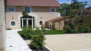 Un bâtiment de couleur beige, avec un toit en tuiles, une entrée centrale et une allée gravillonnée.