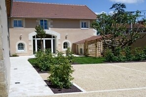 Un bâtiment de couleur beige, avec un toit en tuiles, une entrée centrale et une allée gravillonnée.