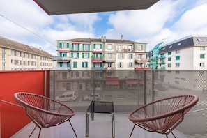 A balcony with two wicker chairs, a table, and a view of a multi-story building with balconies. - The Elegant Minimalist Lakefront (Lausanne)