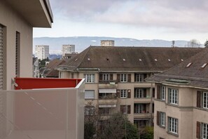 Um edifício residencial com várias sacadas, um toldo vermelho e montanhas ao fundo.