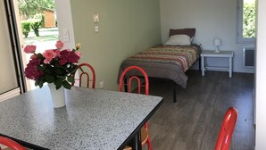 Et værelse med en seng, et bord med en vase blomster, en stol og et vindue.