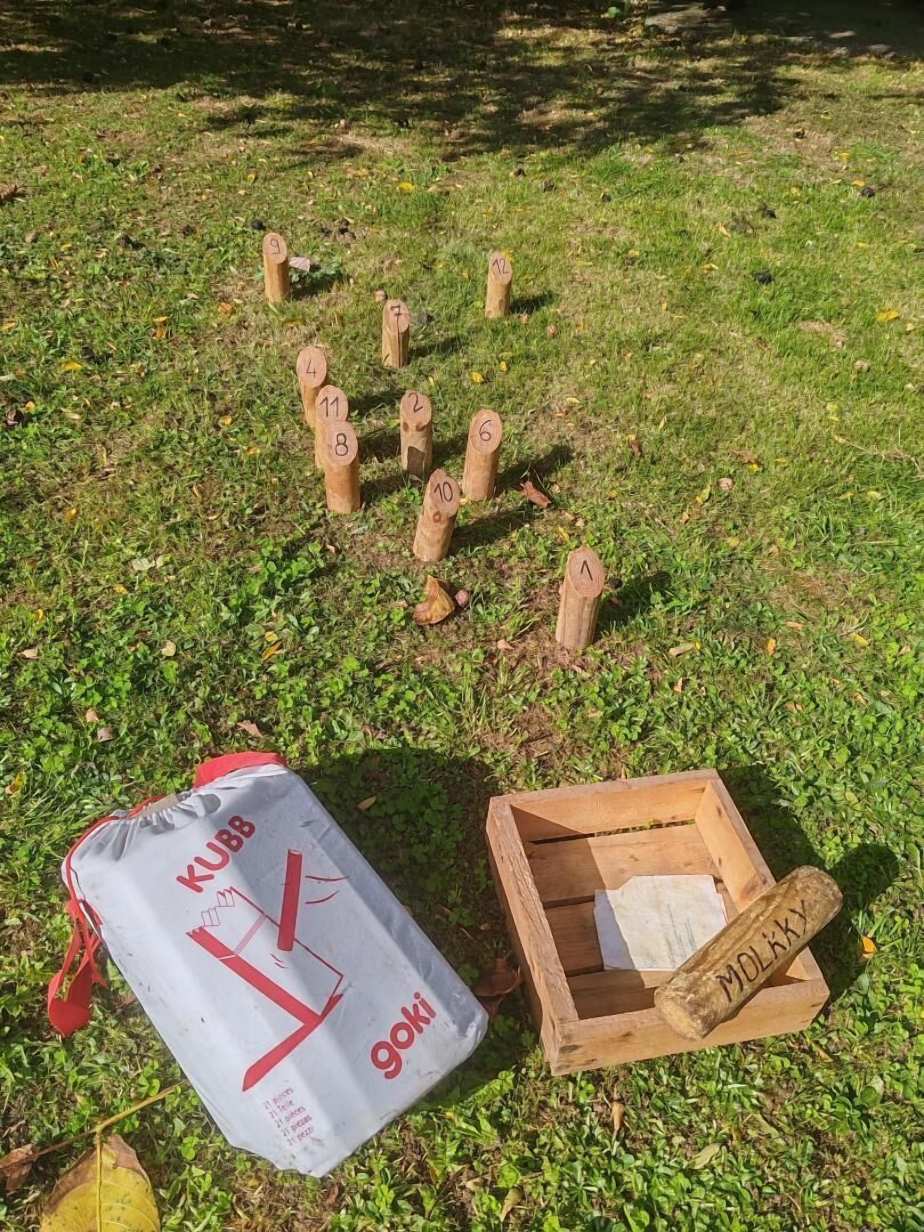Una bolsa con la etiqueta 'KUBB goki' y una caja de madera con la inscripción 'MOLKKX', sobre césped.