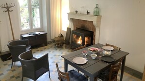 Una habitación acogedora con chimenea, una mesa de comedor, sillas y un ventanal con cortinas.
