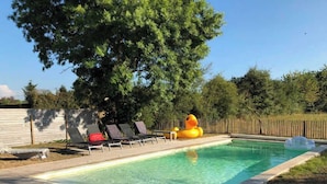 Una piscina rectangular con cubierta de madera, rodeada por una valla de madera y dos sillas de descanso.