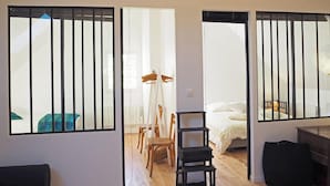 Una habitación con techo de madera, una cama con ropa de cama blanca, una silla, una mesita y una ventana con persianas verticales.