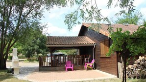 Een houten hut met een overdekt terras, twee stoelen en een barbecue.