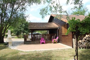 A wooden cabin with a covered patio, two chairs, and a grill. - Le Chalet des Forges (MAIRE)