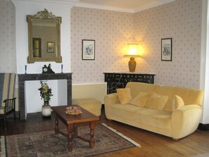 A living room with a sofa, a table, a fireplace, and a mirror. - La Maisons des Tilleuls (THURAGEAU)