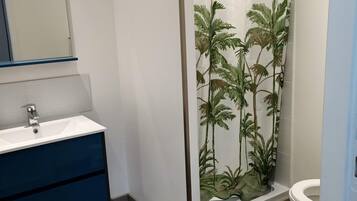 A bathroom with a white sink, a blue cabinet, a glass shower enclosure with a palm tree pattern, and a toilet.