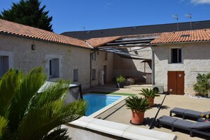 Ein Poolbereich mit einem Steinhaus, Sitzgelegenheiten im Freien und einer überdachten Terrasse.