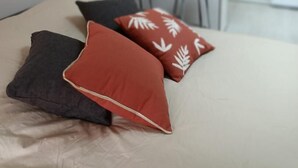 A bed with three pillows, a kitchen area with chairs, and a hanging mirror. - L'écrin - JAUNAY MARIGNY (JAUNAY MARIGNY)