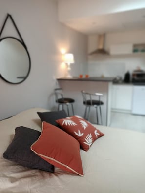 Un lit avec trois oreillers, un coin cuisine avec des chaises et un miroir suspendu.