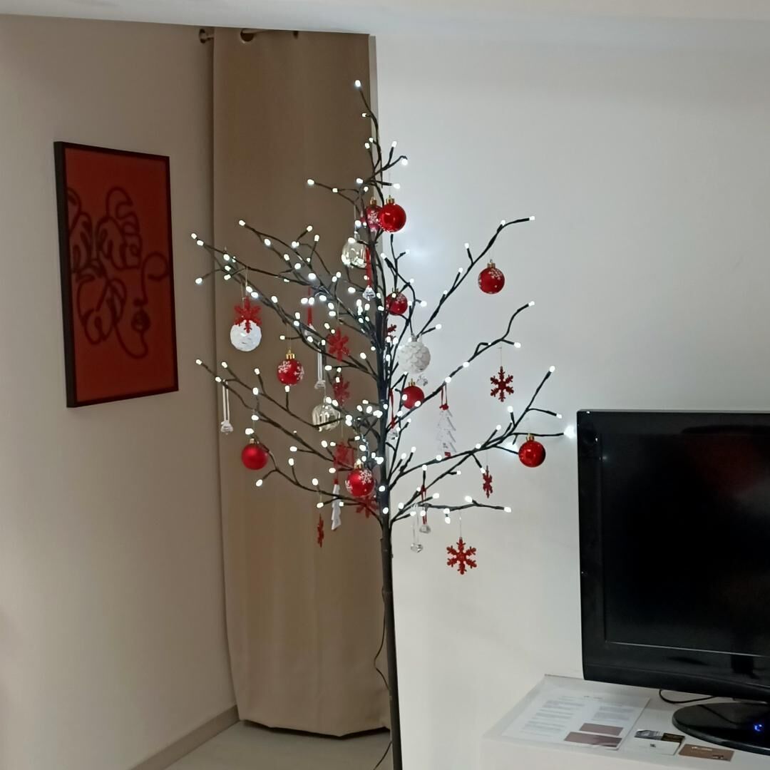 Ett rum med en julgran som är dekorerad med ljus och prydnader, en tv och en inramad tavla på väggen.