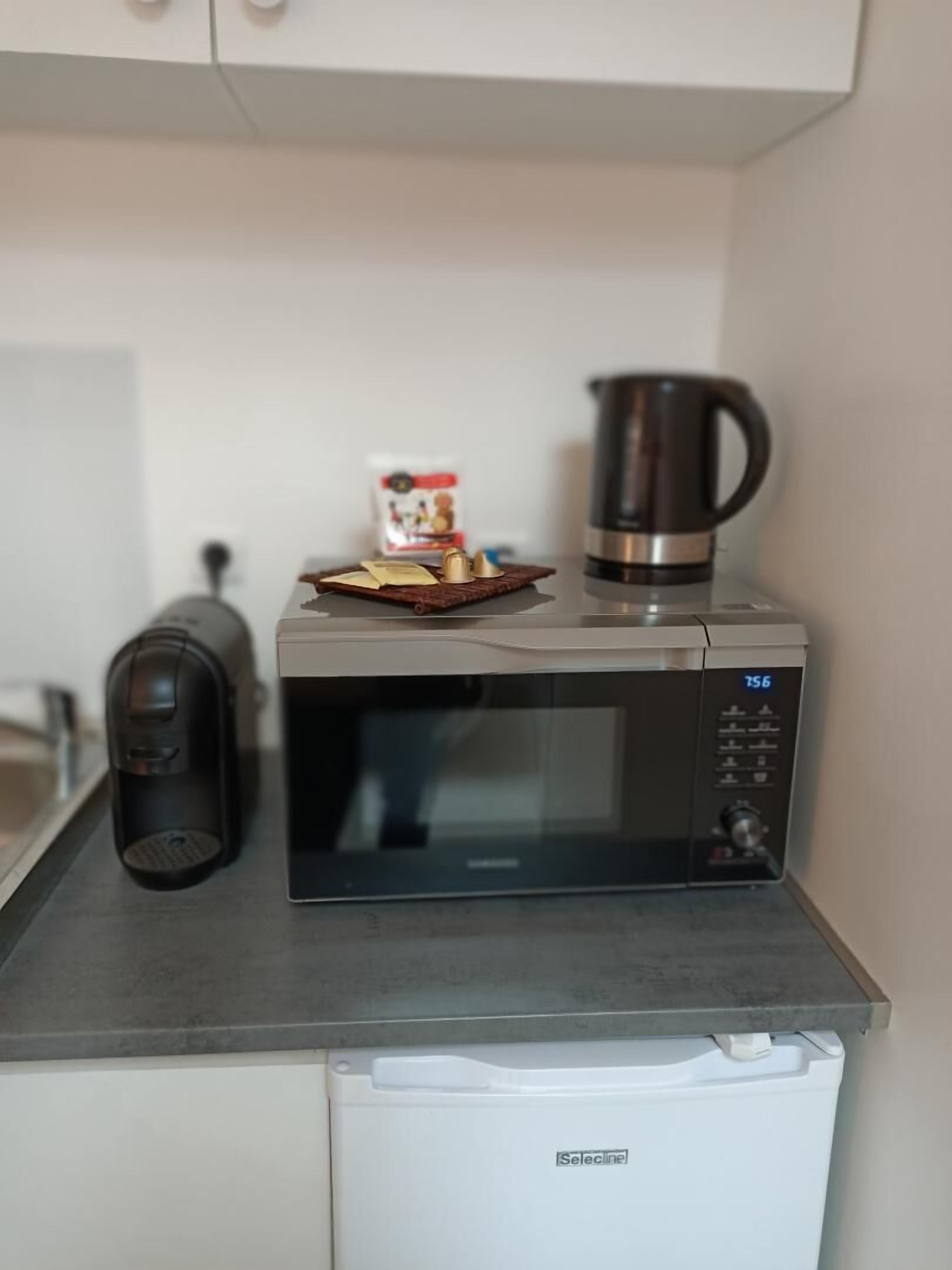 Una cocina equipada con microondas, cafetera y refrigerador pequeño.