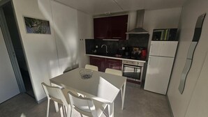 A compact kitchen with white cabinets, a stove, and a refrigerator. There is a dining table with four chairs. - Spotted Woodpecker - SAULGE (SAULGE)