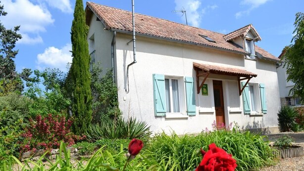 A white house with blue shutters, a tiled roof, and a garden with red roses and greenery. - GITE DE M'et Mme AUGUSTE (VOUNEUIL-SUR-VIENNE)
