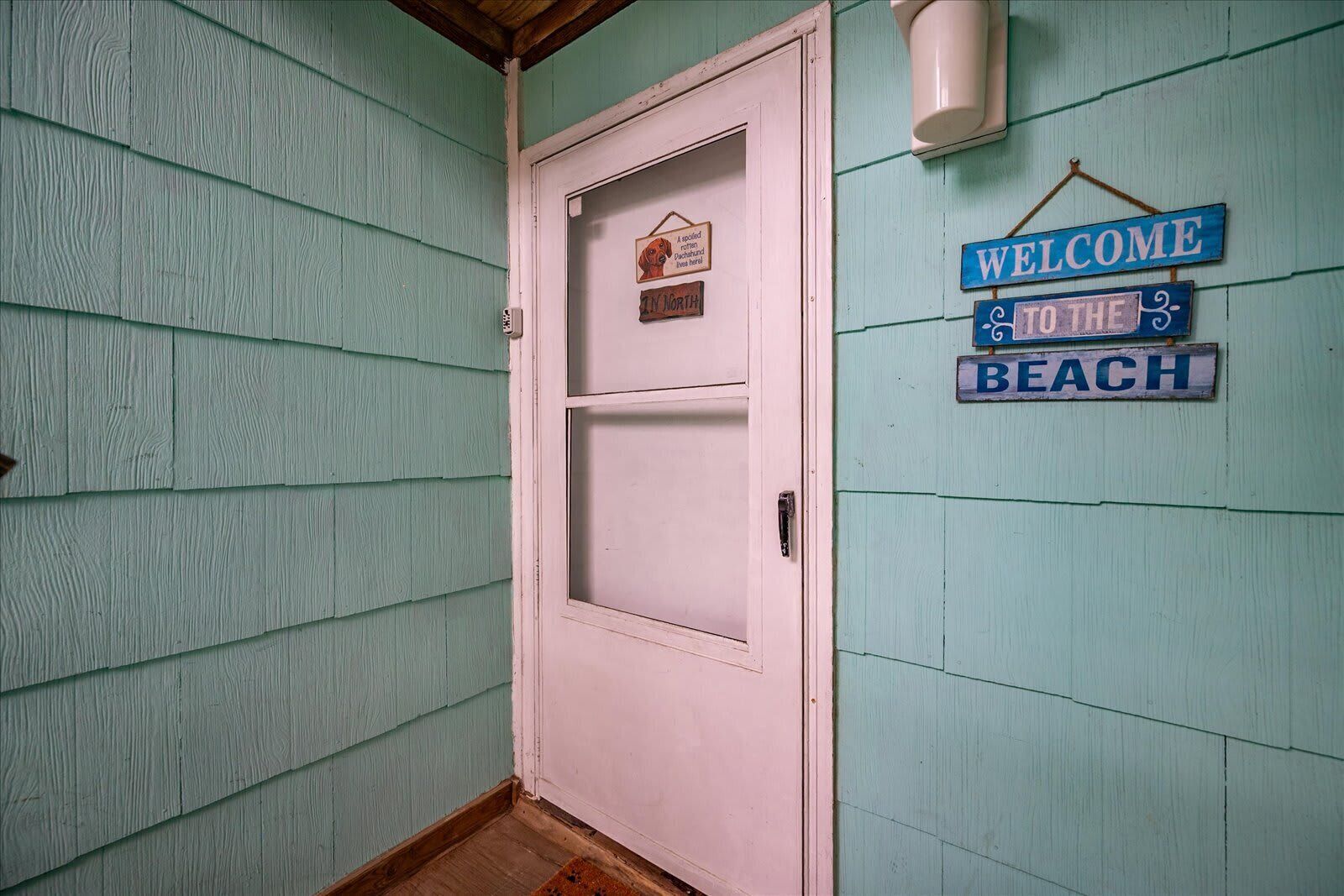 A door with a sign above it, a welcome sign, and a small sign with a dog illustration.