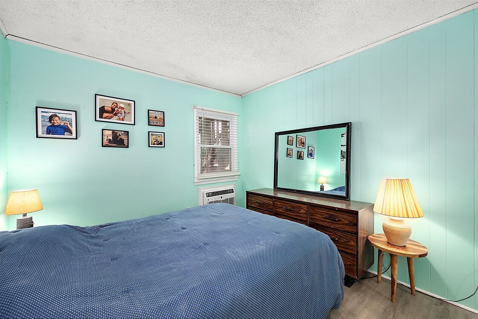 A bedroom with a bed, dresser, mirror, wall-mounted pictures, and two lamps.