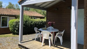 A covered outdoor seating area with a table and chairs, a flower vase, and a wooden deck. - Chalet N° 1 - SAINT SECONDIN (SAINT SECONDIN)