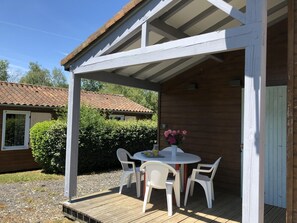 A covered outdoor seating area with a table and chairs, a flower vase, and a wooden deck. - Chalet N° 1 - SAINT SECONDIN (SAINT SECONDIN)