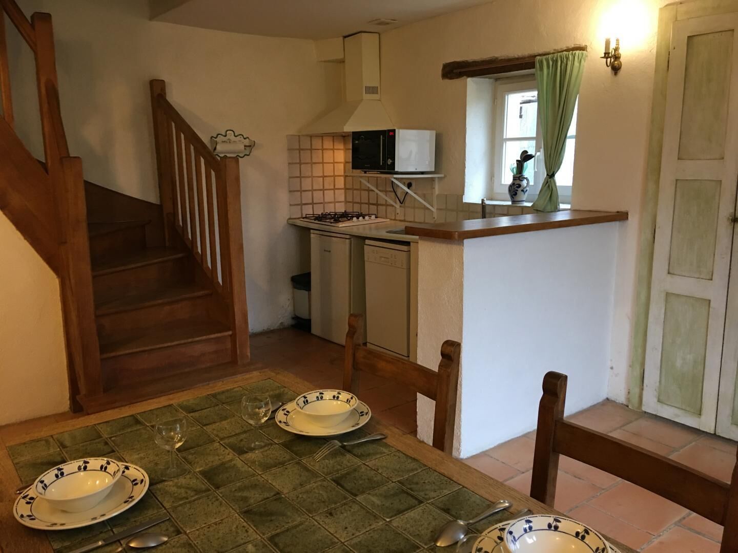 A kitchen with a microwave, stove, and dishwasher. There is a dining table with plates and cutlery. A staircase leads to another room.