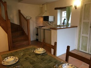 A kitchen with a microwave, stove, and dishwasher. There is a dining table with plates and cutlery. A staircase leads to another room. - Saint-Hubert - OYRE - Gîte (OYRE)