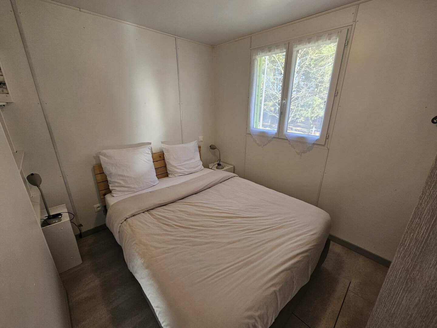 Ein Schlafzimmer mit Bett, Vorhängen am Fenster, einem Nachttisch und einer Lampe.