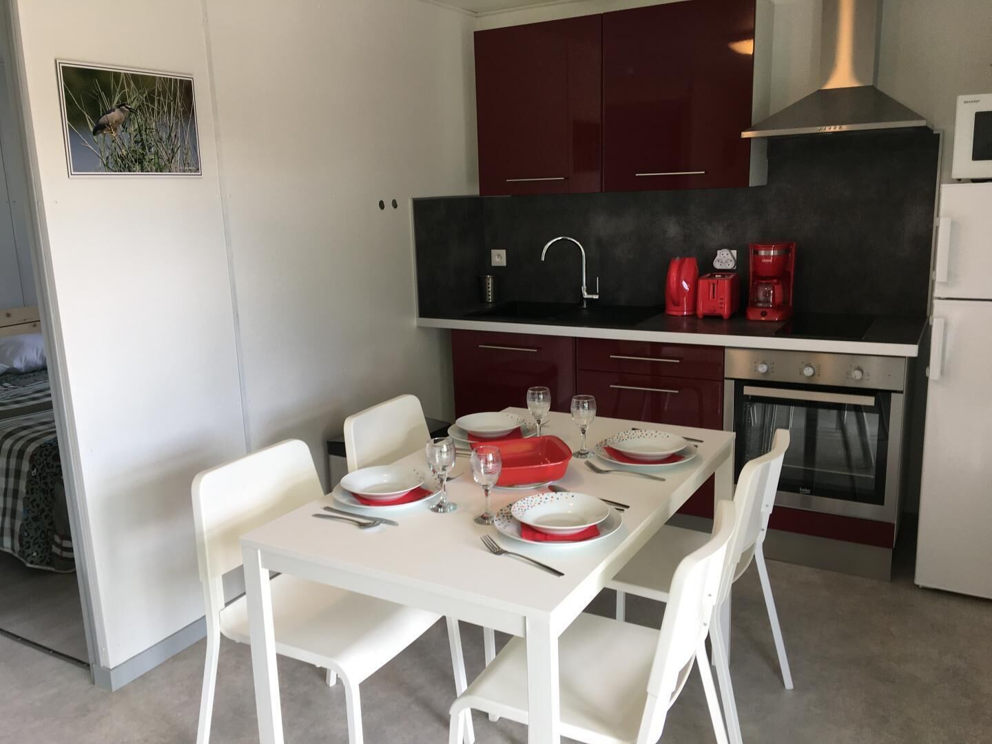 Une cuisine compacte avec une table à manger pour deux personnes, une cafetière rouge et un four encastré.