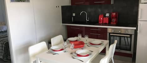 Une cuisine compacte avec une table à manger pour deux personnes, une cafetière rouge et un four encastré.