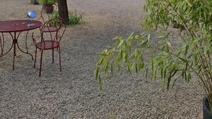 Um pátio com mesa e cadeiras, uma árvore e um edifício com piscina ao fundo.